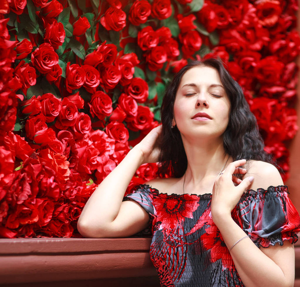 Portrait of elegant dreamy woman in dress on red roses - Фото, изображение