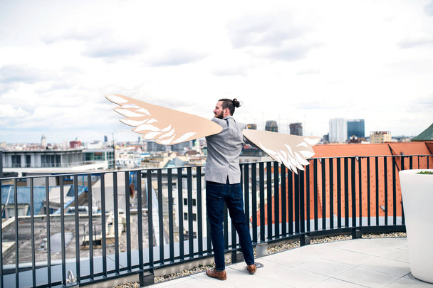 Молодой бизнесмен с крыльями, стоящий на террасе, летающая метафора концепции
. - Фото, изображение