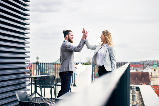 Two young business people standing on a terrace outside office, expressing excitement. - Valokuva, kuva