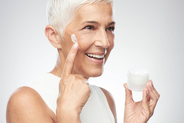 Linda mulher sênior branca sorridente experimentando novo creme anti idade. Fotografia de beleza
. - Foto, Imagem