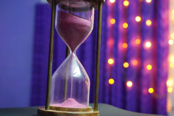 un reloj de arena con arena púrpura clara con fondo bokeh
 - Foto, imagen
