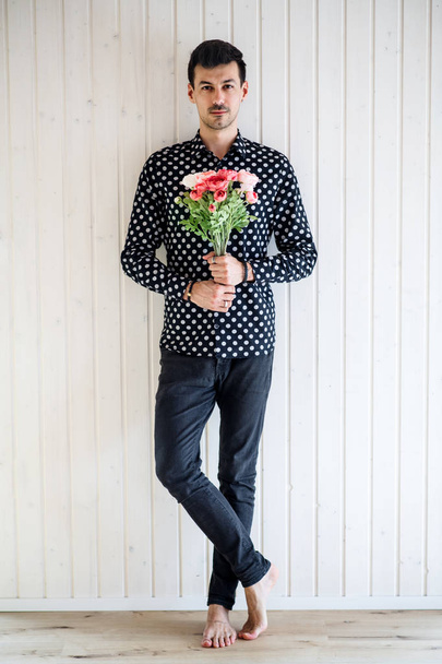 Young man with flowers standing against white wooden background wall. - Фото, изображение