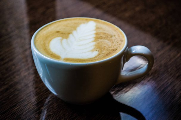 Una tazza bianca di cappuccino con latte art su un tavolo lucido. Rosetta
. - Foto, immagini