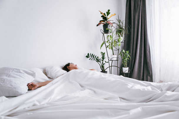 mulher escorregando na cama com lençóis brancos luz solar na janela
 - Foto, Imagem