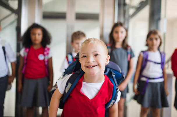 A down-syndrome school boy with group of children in corridor, walking. - Фото, зображення