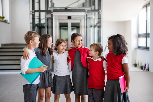 Um grupo de crianças alegres da escola pequena no corredor, olhando para a câmera
. - Foto, Imagem
