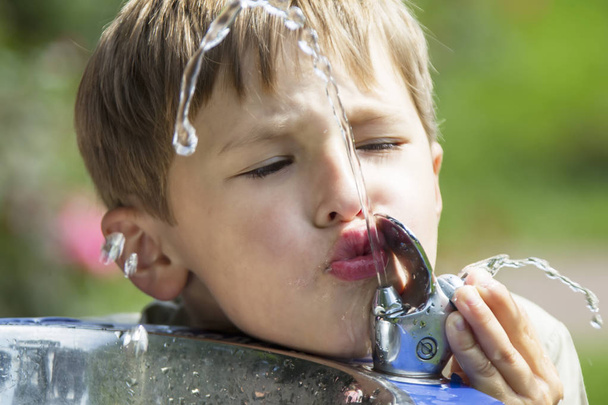 Dítě pije vodu z fontány. Proud vody a pijan. Žízeň. - Fotografie, Obrázek