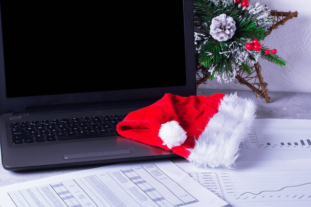 Desktop with laptop and charts. Santa hat  - Photo, image