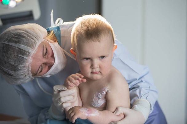 Маленький мальчик-медсестра лечит ожог. Ребенок в больнице ранен. Врач лечит ребенка. Маленький пациент больницы
. - Фото, изображение