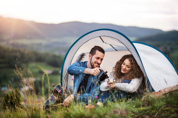 Young tourist couple travellers with tent shelter sitting in nature, drinking coffee. - Foto, Bild