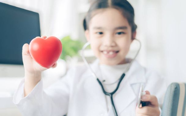 Καρδιά στα χέρια του χαριτωμένο παιδί στο γιατρό παλτό με τη στηθός - Φωτογραφία, εικόνα