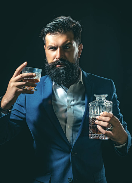 Attractive Bartender in whiskey bar. Stylish rich man holding a glass of old whisky. Man with beard holds glass brandy. - Foto, afbeelding