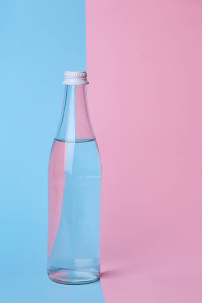 Glass bottle water on a bright pink and blue background close up - Photo, Image