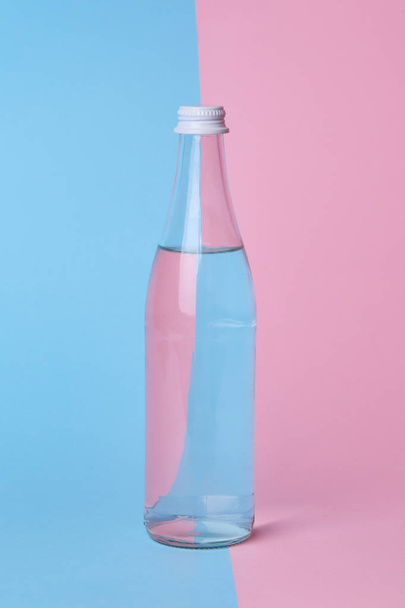 скляна пляшка води на яскраво-рожевому і синьому фоні крупним планом
 - Фото, зображення