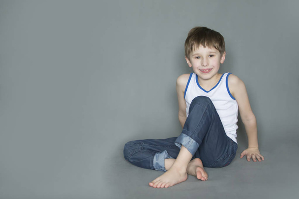 Cheerful preschooler sitting on the floor. Smiling boy in jeans - Foto, imagen