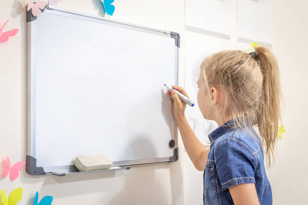 マーカーペンで空のホワイトボードに書いている小さな女の子。学習、教育、コピースペースで学校の概念に戻る - 写真・画像
