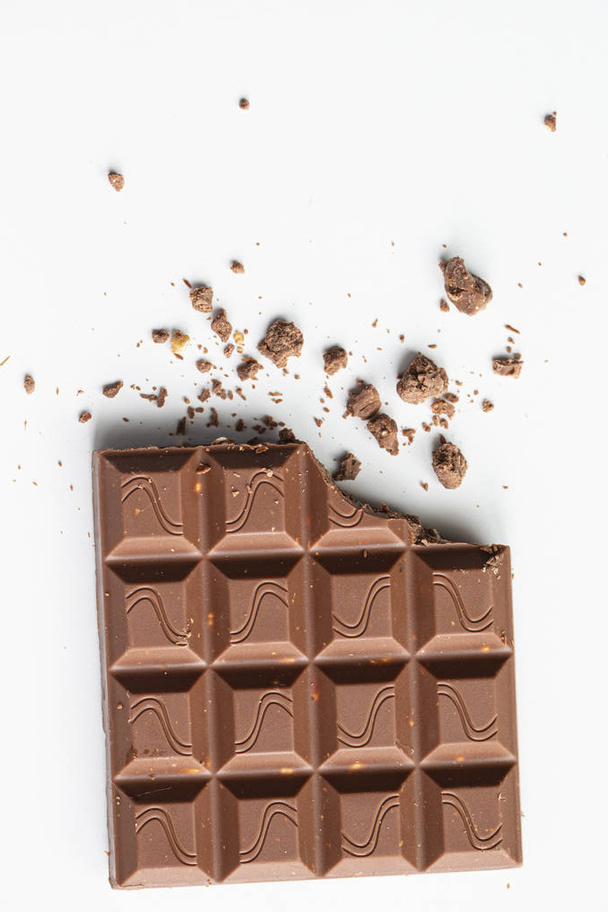 Broken piece of chocolate with crumbs on a white background. Cocoa Dessert - Photo, Image