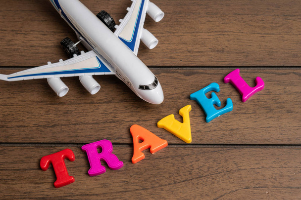 Toy airplane and the word travel made from colorful letters on wooden background - Photo, Image
