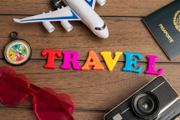 Vliegtuig, kompas, roze hart bril, vintage camera, paspoort en het woord reizen gemaakt van kleurrijke letters op een houten achtergrond - Foto, afbeelding