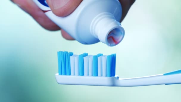 Οδοντιατρική περίθαλψη-συμπίεση οδοντόκρεμα με πολύχρωμες ρίγες από ένα σωλήνα πάνω σε μια οδοντόβουρτσα. - Πλάνα, βίντεο