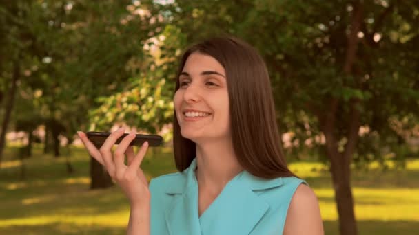 Кавказская девушка вид сбоку с помощью приложения на смартфоне диктует голосовое сообщение снаружи
 - Кадры, видео