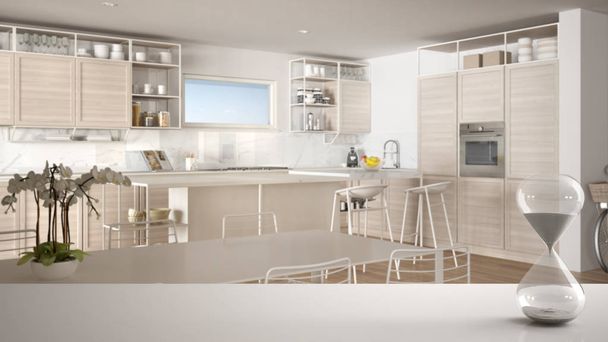 Білий стіл або полиця з кришталевим пісочним годинником, що вимірює час проходження над мінімалістичною білою кухнею з обіднім столом, архітектурний дизайн інтер'єру, копіювання простору фону
 - Фото, зображення