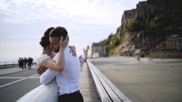 Couple on waterfront at rocks. Action. Newlyweds hugging on waterfront on background of rocks and sky. Bride and groom embrace on background of beautiful scenery quay - Photo, Image