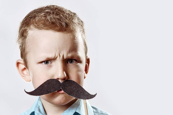 Serious boy with a large moustache frowned against the gray background - Фото, изображение