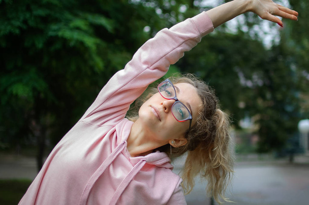 Pembe giysiler ve gözlük aktif fitness kadın ilkbahar veya yaz sabahı sırasında parkta açık germe olduğunu. Sağlıklı yaşam tarzı kavramı - Fotoğraf, Görsel