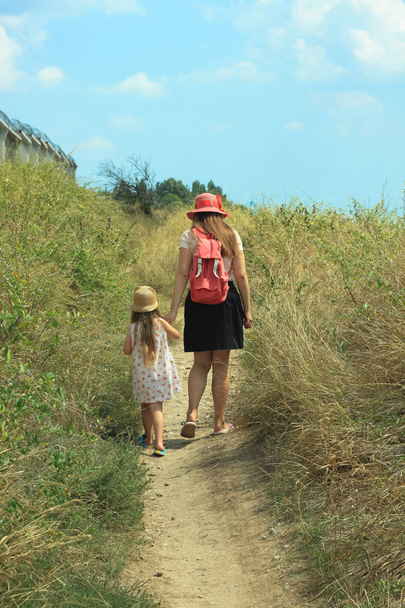Moeder en dochter wandelen in een stro hoeden, geconfronteerd met de camera, genieten van het buitenleven op een mooie dag op de zee en de bergen achtergrond. Reisfotografie. - Foto, afbeelding