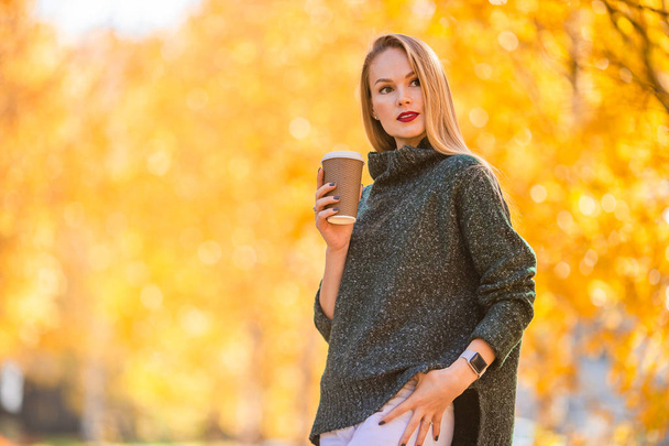 Fall concept - beautiful woman drinking coffee in autumn park under fall foliage - Foto, afbeelding