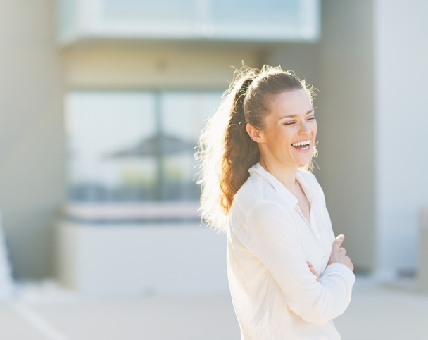 portrét smějící se mladé ženy stojící před dům buil - Fotografie, Obrázek