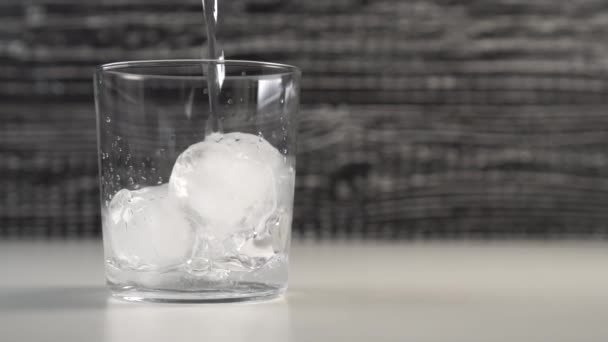 Clear water fills a glass cup with ice cubes. Slow motion. Black and white background - Video, Çekim