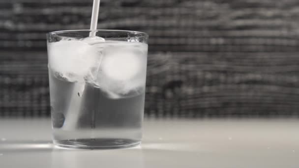 Un bain à boire blanc agite l'eau avec des glaçons dans une tasse en verre. Au ralenti. Fond noir et blanc
 - Séquence, vidéo
