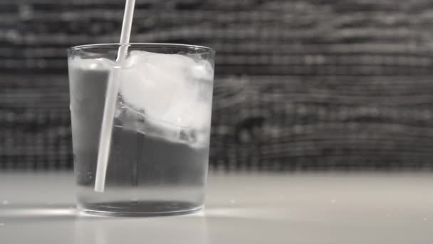 A bartender's hand stirs a drinking tube with ice cubes in a glass cup. Slow motion. Black and white background - Footage, Video