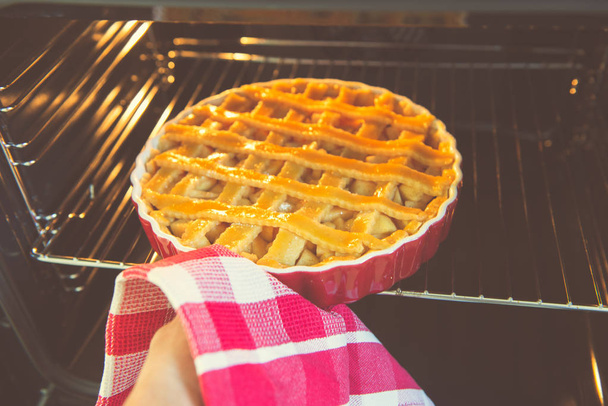Fresh baked golden apple pie in red dish in oven at kitchen  - Photo, image