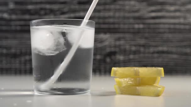 A tube of water and ice in a steamed glass on a black and white background. On the table are slices of fresh lemon - Filmagem, Vídeo