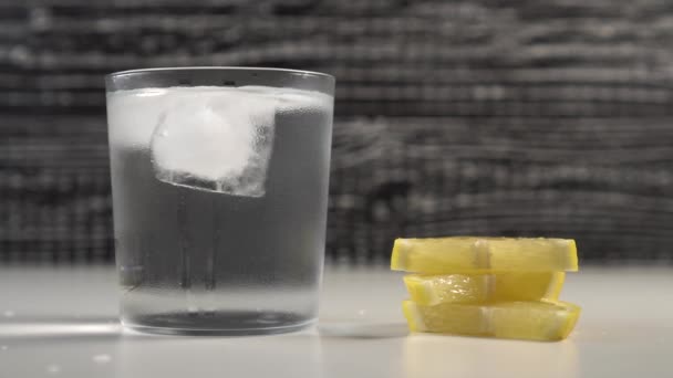 A tube of water and ice in a steamed glass on a black and white background. Man folds slices of fresh lemon - Imágenes, Vídeo