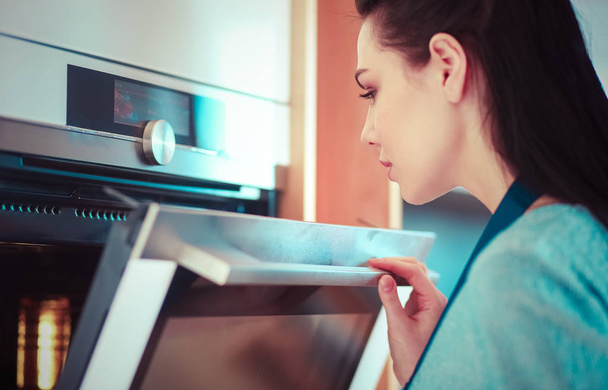Beautiful young woman checking how her cake is doing in the oven - Foto, Imagen