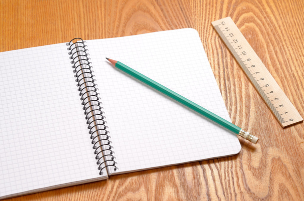 A white note book with lots of room for your text or image and a regular pencil on a wooden desk - Photo, image