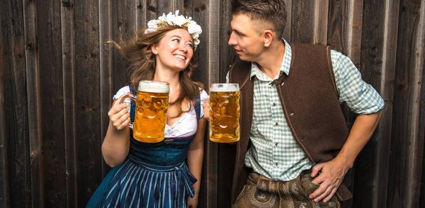 happy young couple in bavarian costumes holding beer glasses, oktoberfest concept - 写真・画像