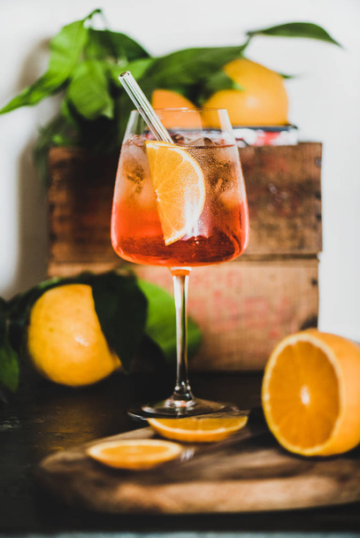 Aperol Spritz aperitif with oranges and ice cubes in glass with eco-friendly glass straw on concrete table, white wall at background, selective focus, close-up. Summer refreshing drink concept - Фото, изображение