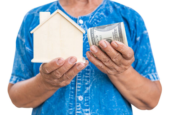 Old farmer woman holding little wood house on a white background. housing and land concept. - Фото, изображение