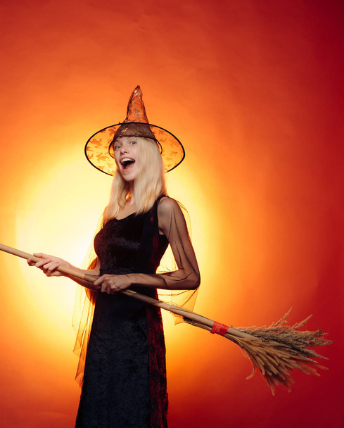 Pretty young blond witch flying on the broom, isolated against orange background. For Text Banner. Halloween design with copyspace. Funny expression. Happy people. Having fun. - Foto, immagini