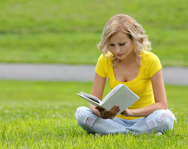 Girl reading the book. Blonde beautiful young woman with book sitting on the grass. Outdoor. Sunny day. Back to school - Foto, immagini