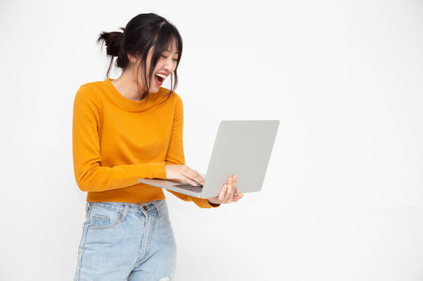 Giovane felice donna asiatica sorridente in abiti casual gialli in possesso di laptop con chiacchierare e ridere con gli amici online
 - Foto, immagini