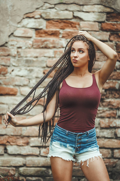 mujer joven con el pelo largo trenzado afro posando sobre fondo de pared de ladrillo
  - Foto, Imagen
