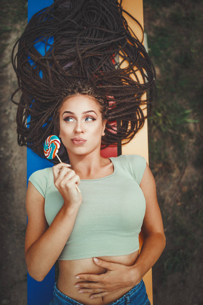 ロリポップを保持する長いアフロ編組ヘアを持つ陽気な若い女性 - 写真・画像