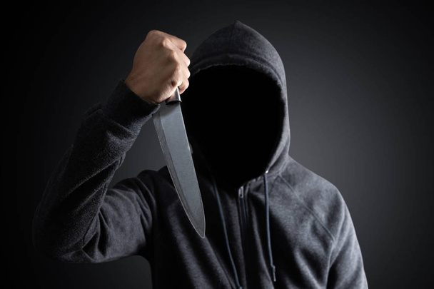Gefährlicher Kapuzenmann steht im Dunkeln und hält Messer in der Hand - Foto, Bild