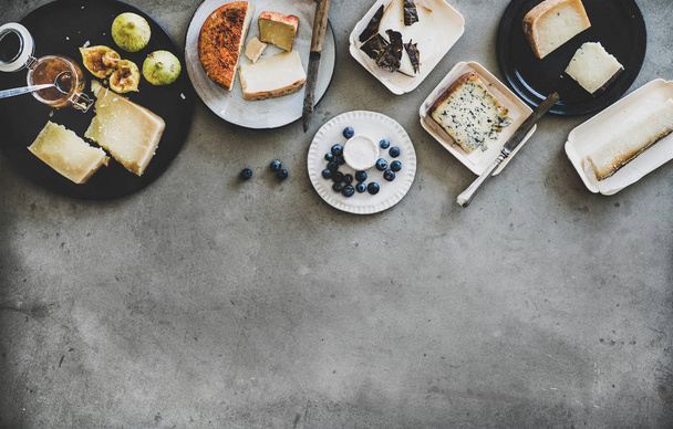Wine snack variety. Flat-lay of cheeses, apricot jam, fresh fruit and crackers over rough grey concrete background, top view, copy space. Gathering, party, holiday food concept - Foto, Bild